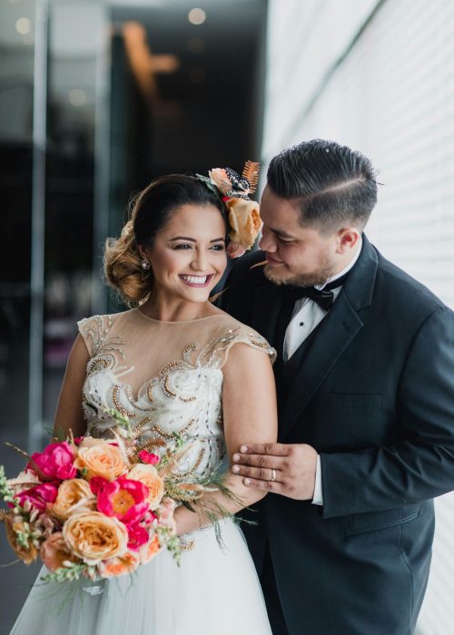 Joyful wedding portrait of a young couple indoors, holding a vibrant bouquet.