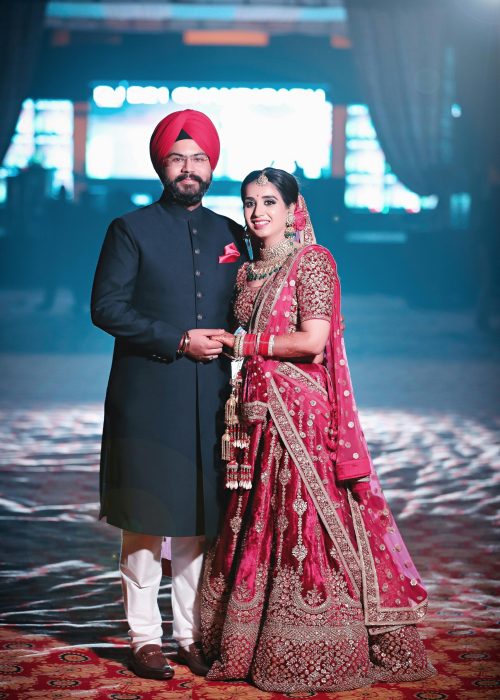 A joyful Indian couple in traditional wedding attire, celebrating their special day indoors.