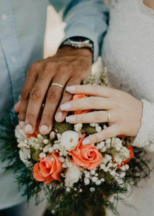 Hands of the bride and groom with wedding rings and floral bouquet, symbolizing love and commitment.